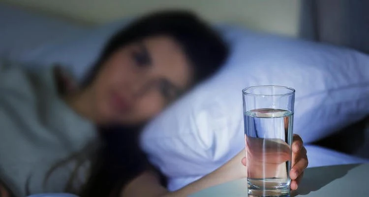 Žena v posteli drží sklenici vody kvůli suchu v ústech