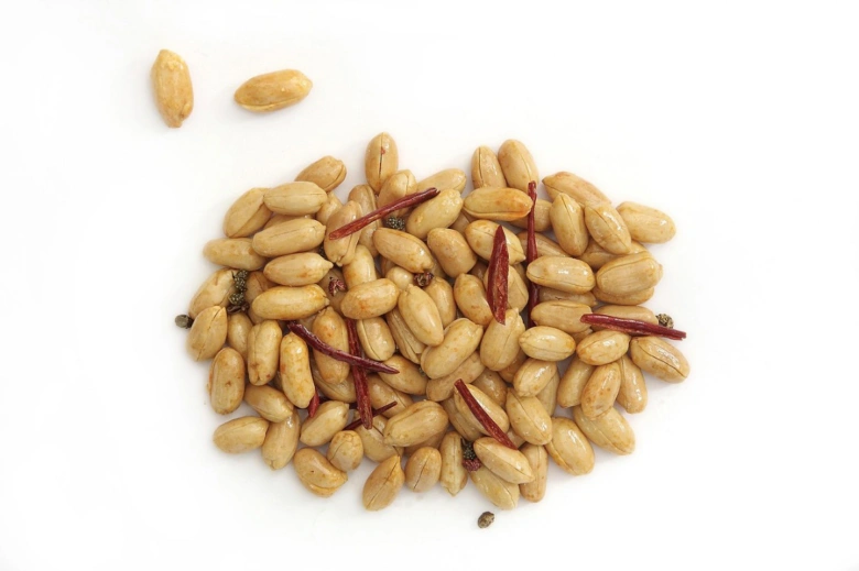 Opravené arašídy s chilli pepřem a kořením na bílém pozadí.