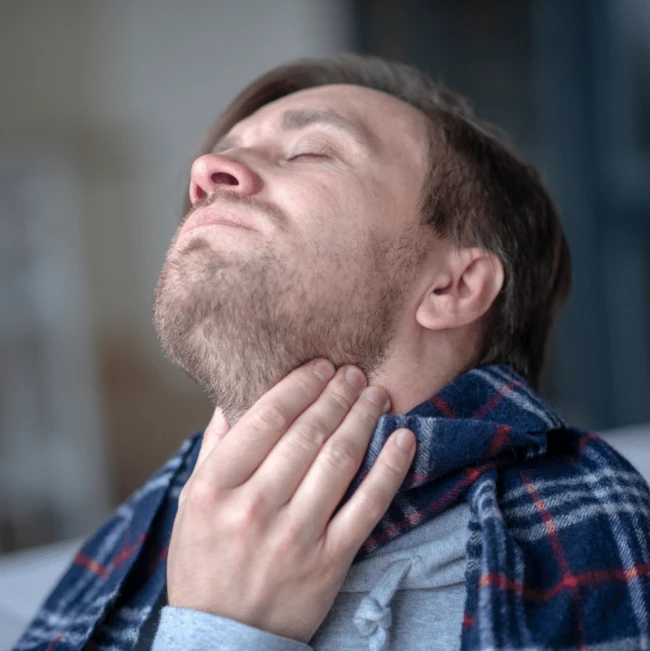 Muž drží krk v bolesti při příznacích angíny.