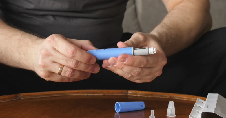 Muž drží modrou injekční tuži pro diabetiky.