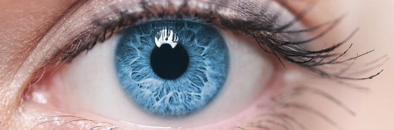 Detailní fotografie lidského oka s modrou zornicí.