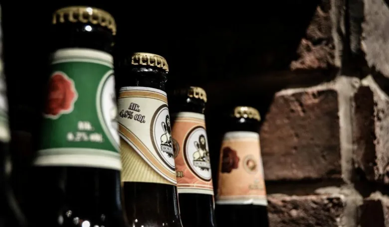 Řada tmavých pivních lahví s viditelným obsahem alkoholu na etiketách.