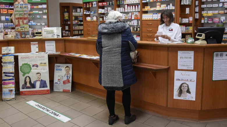 Žena v lékárně konzultuje s farmaceutem u pultu.