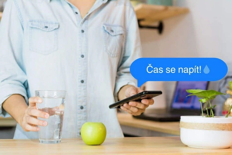 Muž piije vodu z skla s mobilním telefonem.