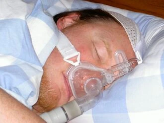 Muž spí s maskou na dýchací soustavu pro léčbu spánkové apnoe.