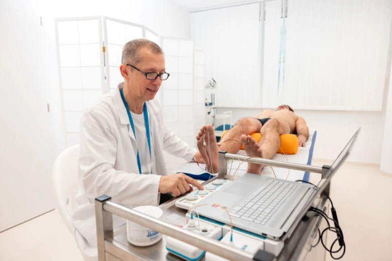 Lékař provádí elektromyografii na noze pacienta v ordinaci.