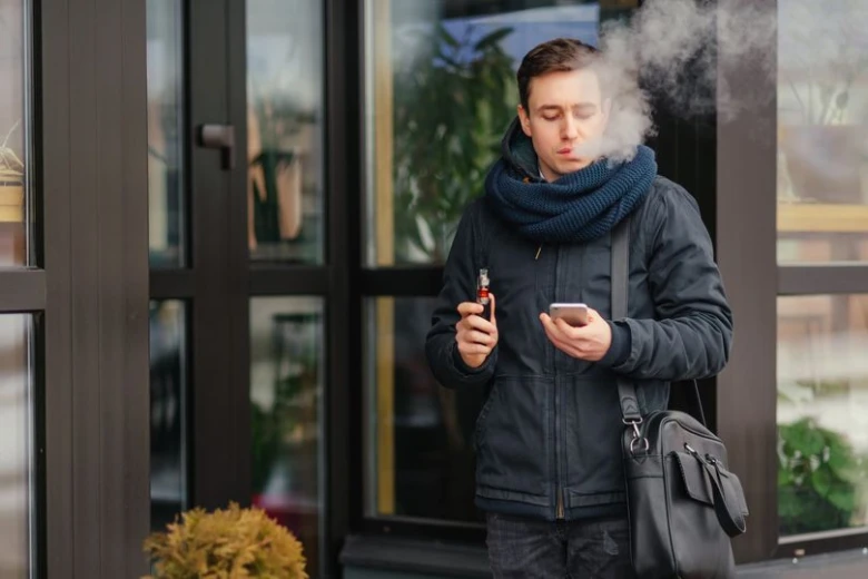 Muž v zimním oblečení vapuje venku před budovou.