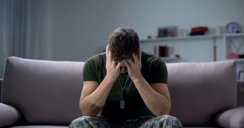 Muž v uniformě sedí na gauči s hlavou dlaněmi.