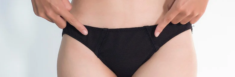 Žena ukazuje na černé kalhotky v oblasti břišní dutiny.