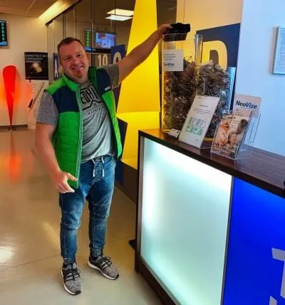 Muž v zelené vestě ukazuje na výstavní skříň s optickými pomůckami.