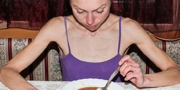 Tenká žena v fialovém tričku jí polévku z talíře.