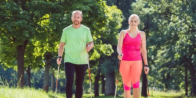 Muž a žena cvičí venku s hůlkami pro nordic walking.