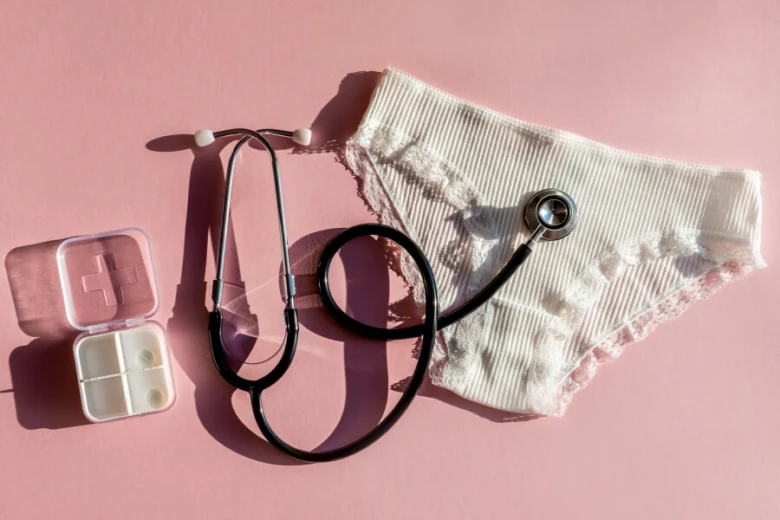 Stetoskop, pilulka a kalhotky na růžovém pozadí pro menstruaci.