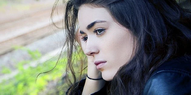 Žena s tmavými vlasy v přemýšlivém postoji venku.