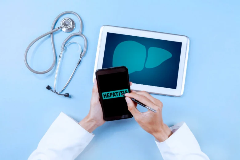 Lékař s tabletem ukazujícím játra, telefonem s textem hepatitida a fonendoskopem.