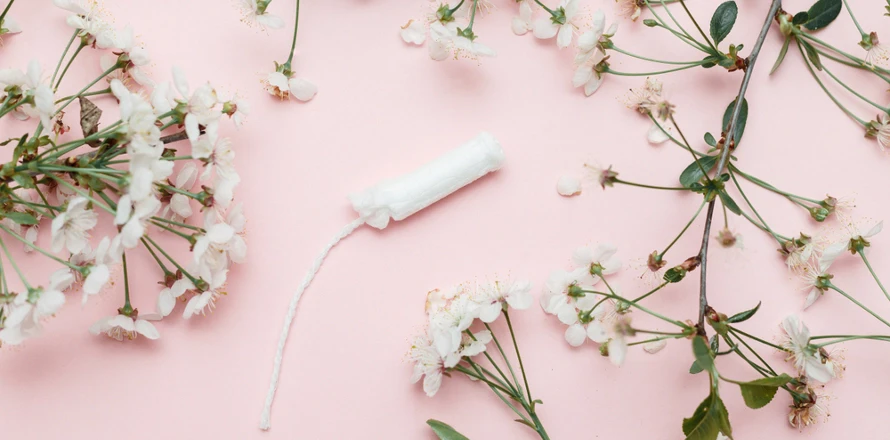 Tampon s vlákny mezi květy na růžovém pozadí