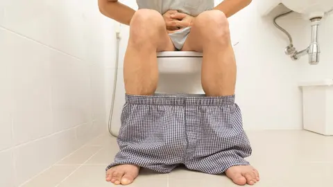 Muž sedí na záchodě s nohavicemi spuštěnými pod kolena.