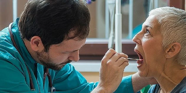 Lékař vyšetřuje hrdlo pacienta nástrojem pro detekci rakoviny krku