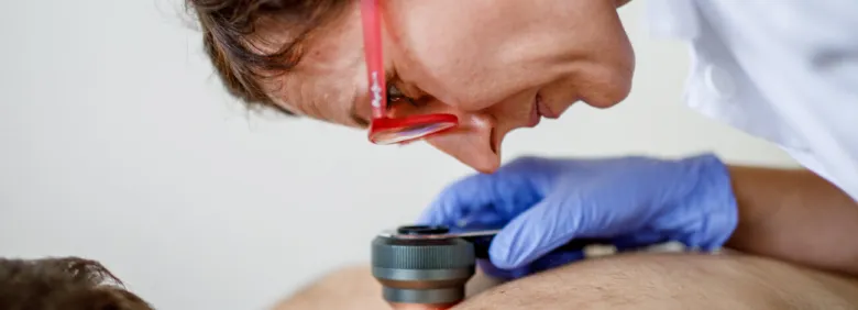 Dermatolog zkoumá kůži pomocí daskopu při vyšetření na rakovinu.