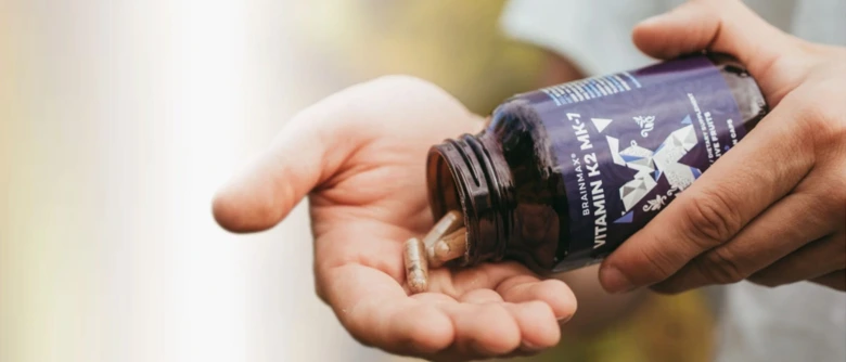 Ruce s lahvičkou vitamínu K2 MK-7 a tobolkami v dlani.