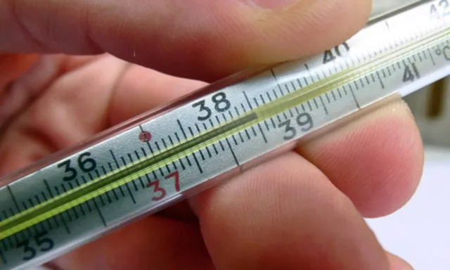Teploměr v ruce ukazující zvýšenou tělesnou teplotu.