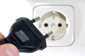 Černá elektrická zástrčka u bílé zásuvky na zdi.
