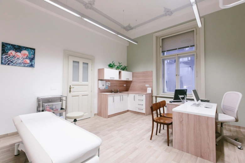Modern lékařský vyšetřovací pokoj s lůžkem a pracovním stolem.