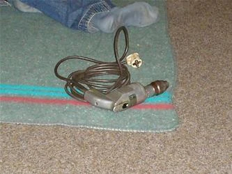 Elektrický vrták leží na zeleném koberci vedle nohou.