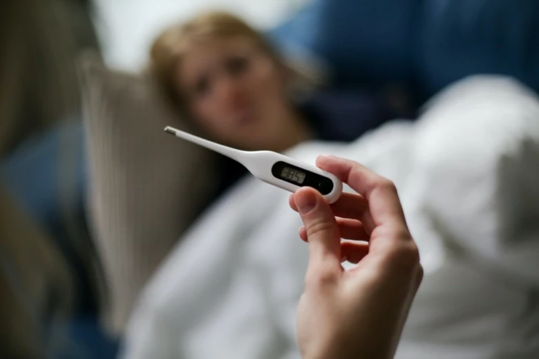 Digitální teploměr ukazující horečku u nemocného člověka v posteli.