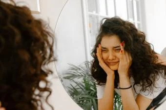 Žena se dívá do zrcadla s výrazem bolesti nebo úzkosti.