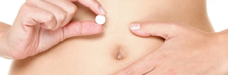 Ruka drží bílou pilulku nad břichem jako prevenci nechtěného těhotenství.
