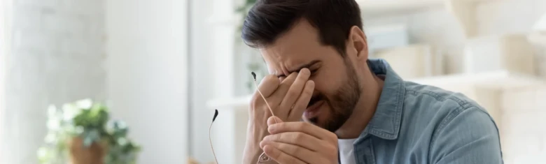 Muž trpící bolestí oka drží si ruku k obličeji.