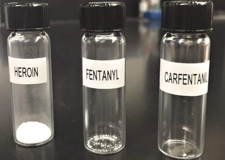 Skleněné lahvičky s bílým práškem označené heroin, fentanyl a karfentanil.
