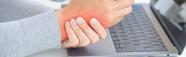 Muž drží bolavou ruku u klávesnice počítače.
