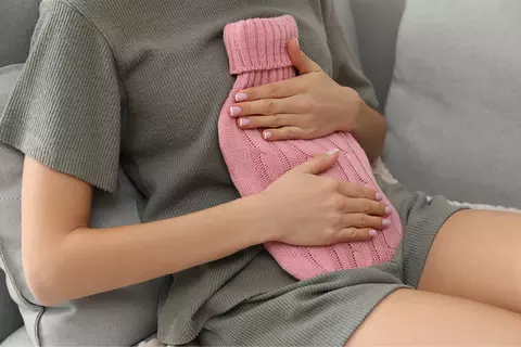 Žena drží na břiše horkou vodu pro úlevu od křečí.