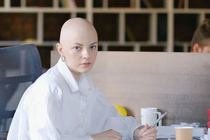 Žena s holou hlavou sedí v kanceláři.