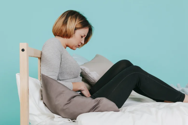 Žena sedí na posteli s bolestí v podbřišku bez menstruace.