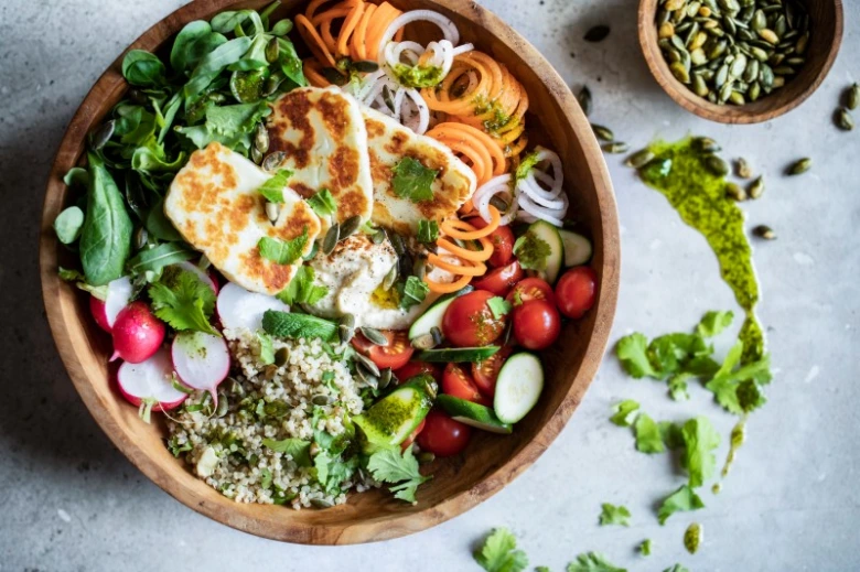 Dřevěná miska s buddhovou miskou obsahující kvinoi a grilovaný halloumi.