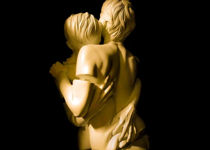 Socha dvou objímajících se postav zezadu na černém pozadí.