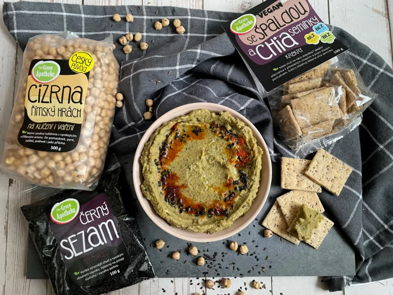 Zelená houmous s cizrny, sezamem a chlebíčky na tmavé podložce.