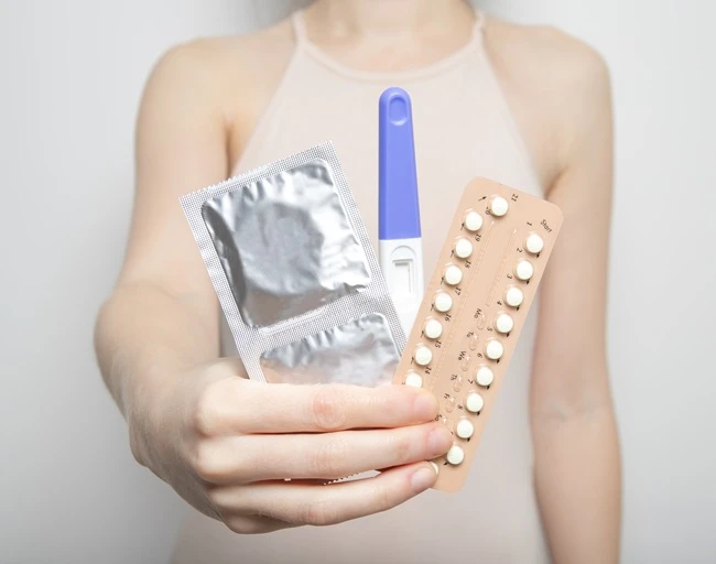 Žena drží kondom, antikoncepční pilulky a těhotenský test.