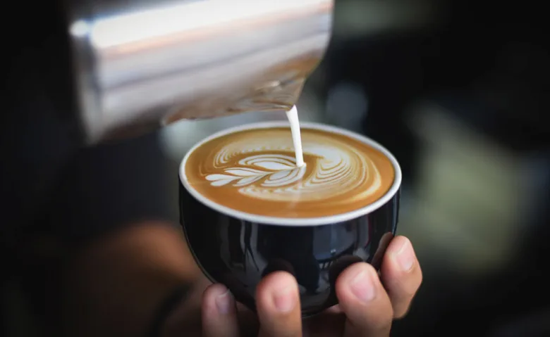 Barista nalévá mléko do šálku s kávou bez kofeinu.