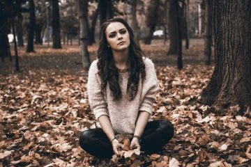 Žena sedí na podlaze v lese s listím.
