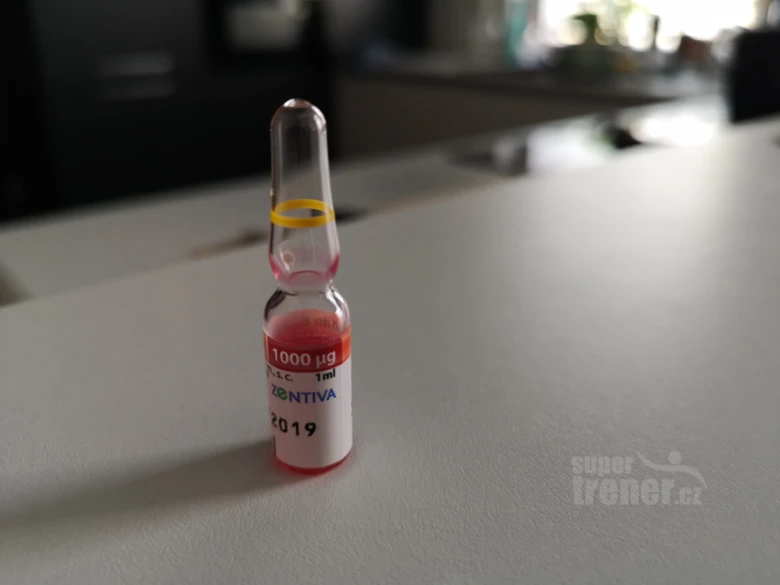 Skleněná ampulka s vitamínem B12 na bílém povrchu.