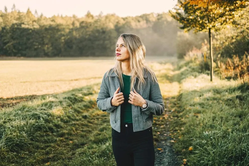 Žena stojí venku v přírodě s myšlenkami o stresu.