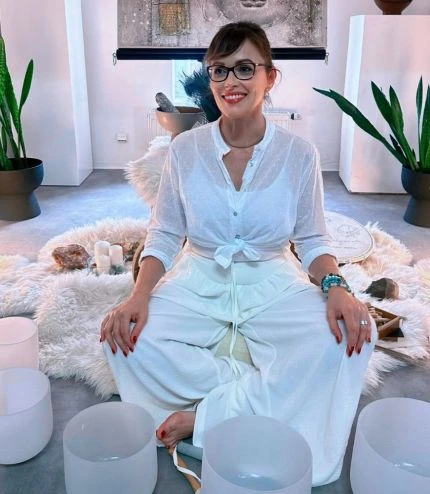 Žena sedí na koženém koberci s krystaly a zpívajícími miskami.