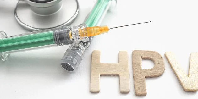 Střiková jehla s HPV vakcínou vedle dřevěných písmen.