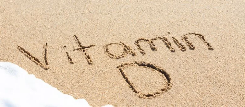 Slova Vitamin D vyrytá v písku na pláži.
