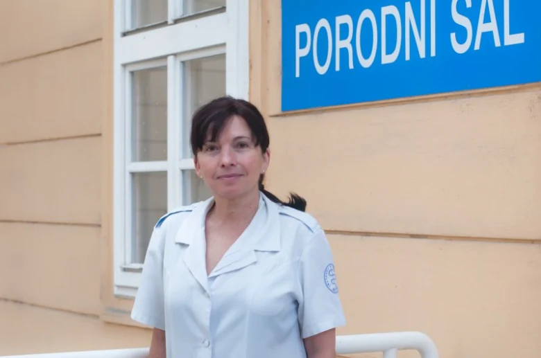 Sestra stojí před budovou porodní místnosti.