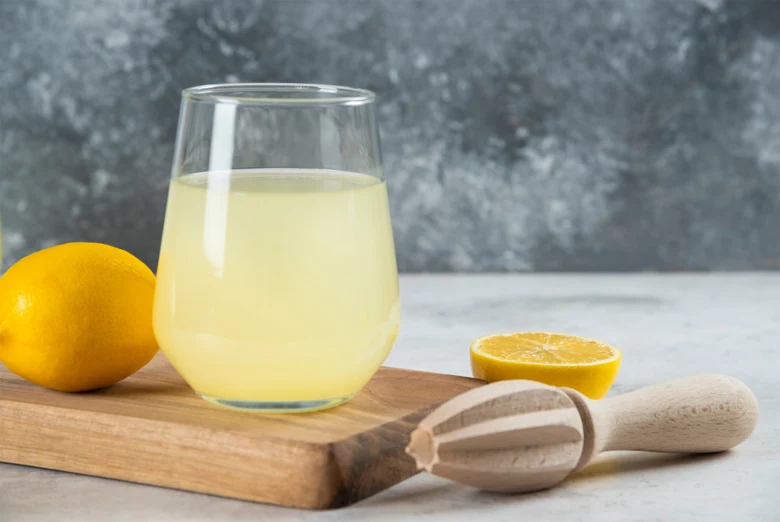 Sklenice citronové šťávy s lisem na dřevěné desce.